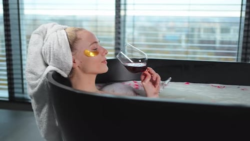 Spa Relaxation Woman Lying in Bath with Holding Glass with Red Wine Girl Relaxing in Bathroom at