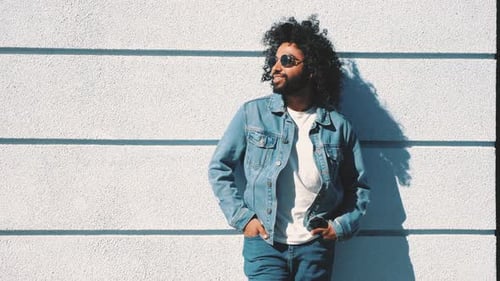 Stylish Man with Curly Hair Posing by Wall