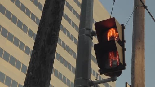 Pedestrian light flashing from walk to stop with with a time countdown, a building and grayish sky i