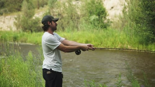Caucasian man fly fishing in fast-flowing river, lush green river bank