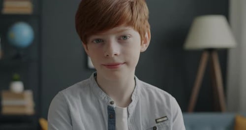 Portrait of Pensive Boy with Red Hair Looking at Camera Indoors in Apartment