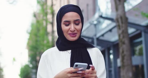 Woman Smiling and Using Smartphone in City