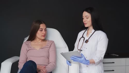 A Doctor in a White Coat Consults a Young Female Patient in the Office of a Private Clinic The