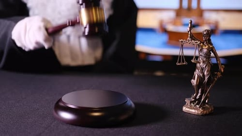 Judge Hand with a Gavel Hitting the Sound Block Next to a Justice Statue Symbolic Legal Decision