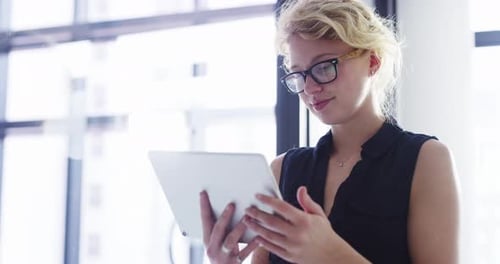Imágenes de vídeo en 4K de una atractiva joven empresaria usando su tableta mientras trabaja en la oficina