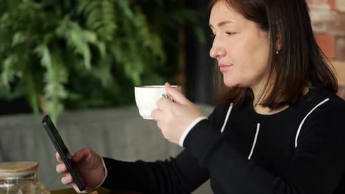 Woman Drinking Tea and Using Smartphone in Cafe