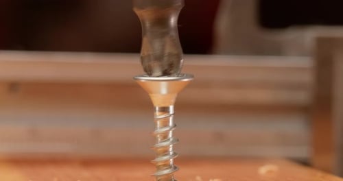 Close-up is an electric drill the screws a self-tapping screw into a wooden bar.