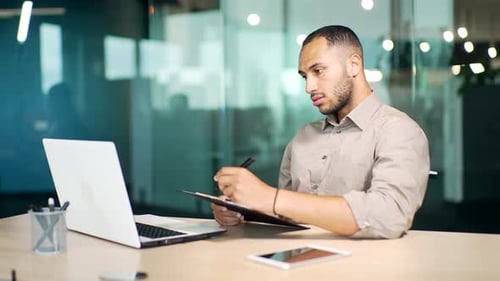 Focused businessman manager watching educational video on computer, writing notes in copybook