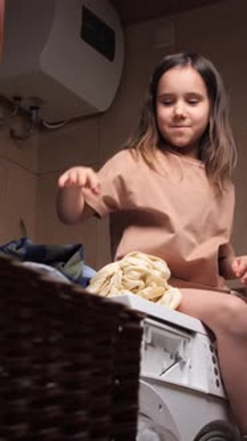 Vertikales Video: Ein lächelndes junges Mädchen, das auf einer Waschmaschine sitzt und ein kariertes Hemd hält