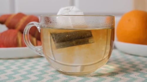Tea Bag Steeping in Glass Cup with Croissants