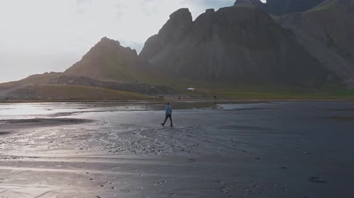 Person Walking on Reflective Black Sand Beach with Stokksnes Peaks