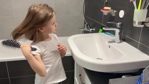 Girl brushes her hair in the bathroom