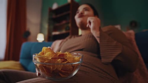 African American Woman Eats Chips Watching TV in Evening