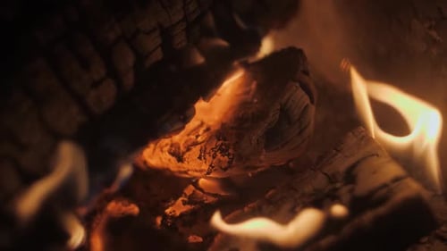 Fire in a fireplace in slow motion with pieces of wood through a tiled grill