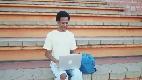 Young afro non-binary student using laptop on campus