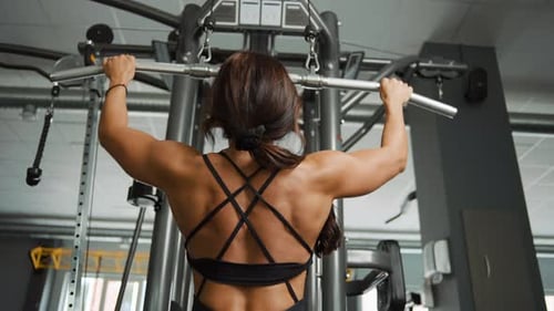 Beautiful sporty young woman training back muscles in gym