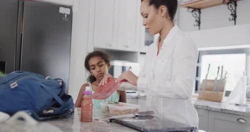 Happy african american mother and daughter packing lunch for school in kitchen, slow motion