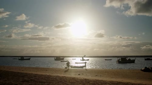 Silhouette zweier Männer, die ein kleines Ruderboot zum Angeln vorbereiten, und einer Person, die im Sand spaziert