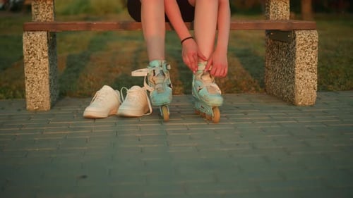 Dame retirant la sangle de son patin à roulettes sur un banc avec des baskets au coucher du soleil