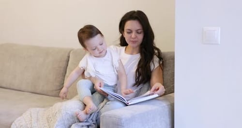 Mother and Child Reading Picture Book Together on Sofa