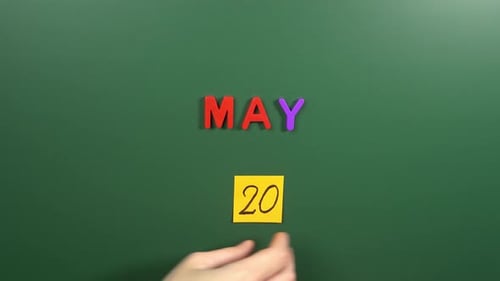 Hand sticking a sticker 20 May calendar day on school board. 20 date of May. Twentieth day May