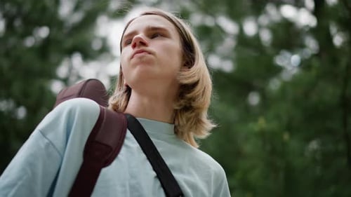 Thoughtful Young Man Outdoors with Guitar Case