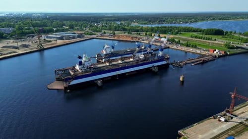 A View of a Shipyard Featuring Large Vessels on Floating Dry Docks Beside a Calm Harbor - Aerial Dro