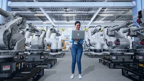 Smiling Woman Working with Robots in Modern Factory
