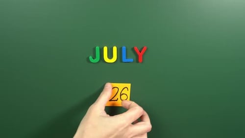 Hand sticking a sticker 26 July calendar day on school board. 26 date of July. Twenty sixth day