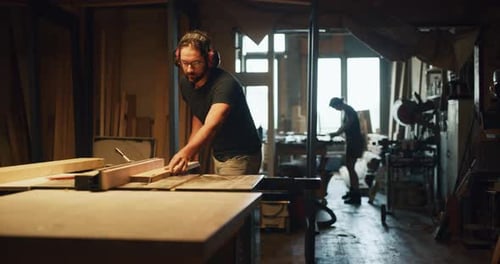 Carpenter cuts wood on table saw in warm light atelier with red camera footage