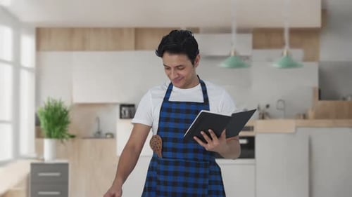 Smiling Man Cooking with Cookbook in Modern Kitchen