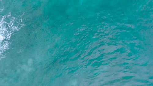 Top Down Slow Motion Drone View of turquoise clear water and crashing waves over shallow coral reef