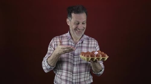 Man Holds and Examines a Container of Eggs