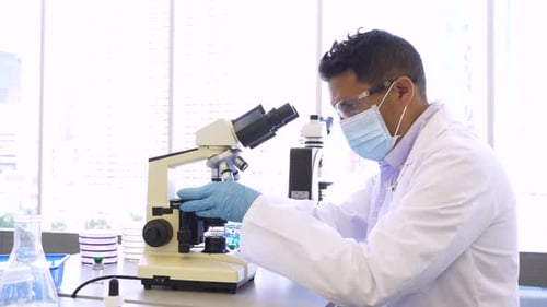 Male Scientist In Face Mask Using Microscope In Science Laboratory