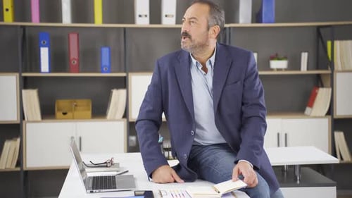 Man Sitting on Desk with Laptop in Office