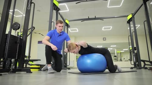 Woman Exercises on Ball with Trainer in Gym