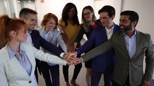 Diverse businesspeople joining hands in an office, showcasing unity and collaboration. Smiling faces
