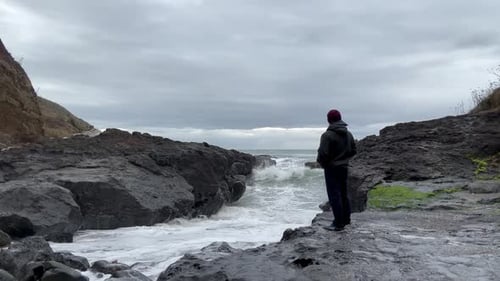 Lonely Man At The Rocky Shore With Breaking Sea Waves During Cloudy Day. Static Shot
