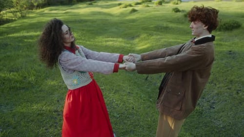 Young Loving Couple Holding Hands and Smiling in Green Field