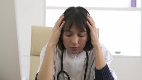 Stressed female doctor suffers from headache in clinic