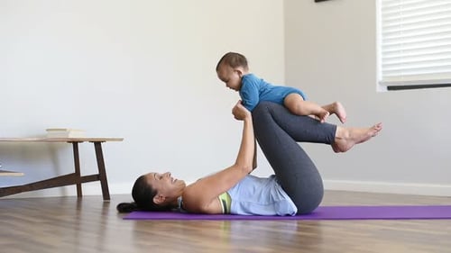 Athletic hispanic mother doing gymnastics with little son on yoga mat at home