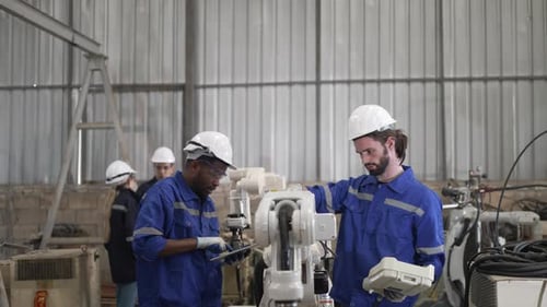 Blue collar workers are working at machine shop with welding robot arm.