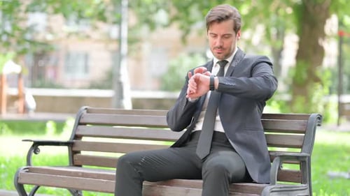 Young Adult in Suit Checks Smartwatch on Bench