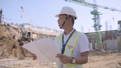 Construction Engineer Reviews Blueprints at Construction Site