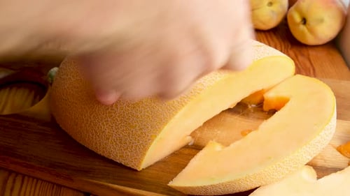 Mann schneidet reife gelbe Melone auf einem Holzschneidebrett mit einem scharfen Küchenmesser in Stücke Juicy