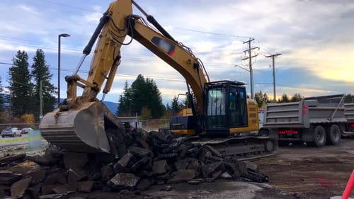 Excavator Loading Asphalt into Dump Truck on Construction Site