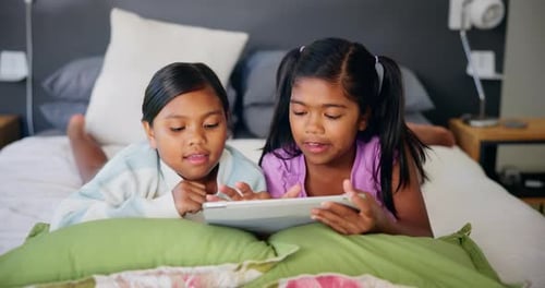 Two Girls Using Tablet Device on Bed