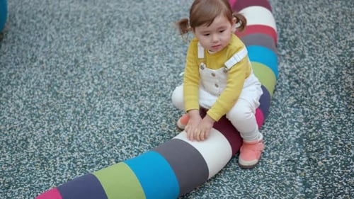 Happy 3-Year-Old Toddler Girl Sitting On Colorful Soft Long Pillow At The Play Area Inside A Shoppin