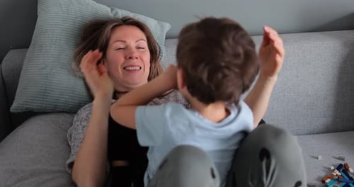 Young Mother Fool Around with Five Year Old Lough Son on Sofa at Home