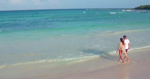 Young Couple Walks Into Waves on Tropical Beach by Aerial Drone Attractive
